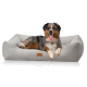 Ein glücklicher Australian Shepherd Hund, der auf einem plüschigen, grauen Haustierbett mit strukturierter Oberfläche und einem kleinen Lederschild entspannt.