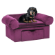 Ein schwarz-brauner Dackel sitzt bequem auf einem plüschigen lila Hundesofa mit abgerundeten Armlehnen und einer Schublade darunter.