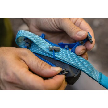 Eine Nahaufnahme von Händen, die einen blauen Haustiergeschirrriemen mit grauen Clips anpassen, wobei die Textur des Stoffes und der Hardware gezeigt wird.