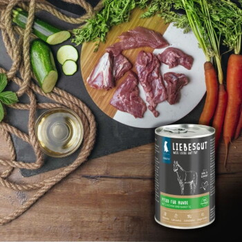 Dose LIEBESGUT-Hundefutter mit der Aufschrift 'Pferd für Hunde' neben rohem Pferdefleisch auf einem Brett, Karotten, Zucchini und einer kleinen Schale Öl.
