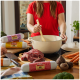 Person rührt in einem Topf mit DIBO Rohfutter-Packungen und frischem Fleisch, Karotten und Gemüse auf einem Küchentisch.