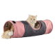 Een fluffy oranje kat kijkt vanuit een roze en grijze stoffen tunnel, met een pompon-speeltje zichtbaar binnenin.