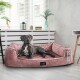 Ein schwarzer Hund liegt auf einem plüschigen rosa Hundebett mit einem Etikett, das "tierlando" beschriftet ist, in einem hellen Raum mit weißen Jalousien und dekorativen Pflanzen.