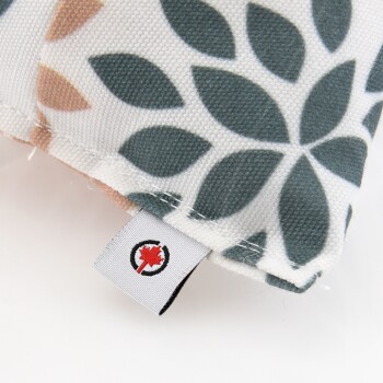 Nahaufnahme einer Ecke eines Haustierbettes mit einem floralen Muster in Türkis und Pfirsich, mit einem sichtbaren Markenschild, das ein Ahornblatt-Logo zeigt.