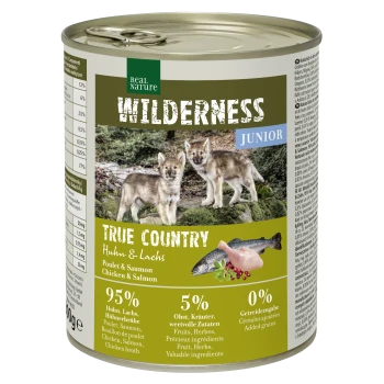 Eine Dose Real Nature Wilderness Junior Haustierfutter mit zwei Wolfshunden, beschriftet mit "95 % Huhn & Lachs, 5 % Früchte & Kräuter, 0 % Getreide."
