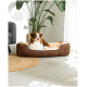 Ein brauner und cremefarbener Australian Shepherd-Hund, der in einem plüschigen Haustierbett entspannt, umgeben von Zimmerpflanzen und einem grauen Sofa.