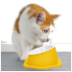 Eine neugierige orange-weiße Katze lehnt sich zu einer hellgelben Futterschüssel mit weißem Innenraum, die auf einem grauen Boden steht.