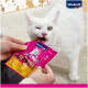 Eine Person hält ein pinkes Paket von Vitakraft Cat Snack, während eine weiße Katze gierig einen Leckerbissen daraus beißt, was die Markenidentität und den Inhalt des Produkts zeigt.