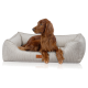 Ein brauner Irish Setter, der bequem in einem plüschigen, beigen Haustierbett mit strukturiertem Stoff und einem kleinen Lederetikett liegt.