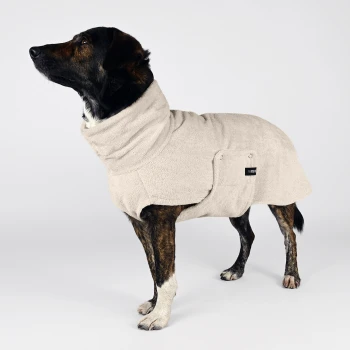 Ein Hund trägt einen weichen beigen Fleece-Mantel, steht stolz mit erhobenem Kopf und zeigt eine Tasche an der Seite sowie ein Markenlabel.