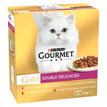 White fluffy cat with green eyes on a gold box of Purina Gourmet Gold Double Delicacies cat food, featuring various flavors.