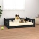 Ein Collie-Hund liegt auf einem cremefarbenen Haustierbett mit einem schwarzen Holzrahmen, neben einem grünen Tennisball auf einem Holzboden.