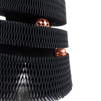 Ein modernes schwarzes Katzenspielzeug mit Wabenmuster, das zwei orangefarbene Bälle zeigt, die durch die Schichten blitzen.