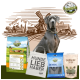 Ein grauer Hund sitzt neben BELLEFOR Tierprodukten: blaues Hundefutter, eine weiße Tragetasche, Zahnsticks und Hautergänzungen, mit einer ländlichen Kulisse.
