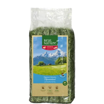 Wiesenheu Alpenvorland 1,5kg Eine durchsichtige Plastiktüte gefüllt mit grünem Heu, beschriftet mit "Real Nature" und einer malerischen Berglandschaft im Hintergrund.