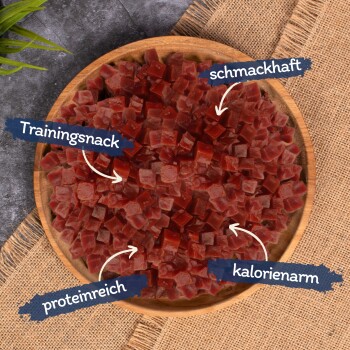 Eine Holzschüssel mit gewürfelten roten Hundeleckerlis, beschriftet auf Deutsch: "Trainingssnack", "schmackhaft", "proteinreich" und "kalorienarm".