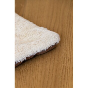 Ein weiches, plüschiges Haustierbett mit einer cremefarbenen Oberseite und einer braunen Unterseite, das auf einer Holzoberfläche ruht.