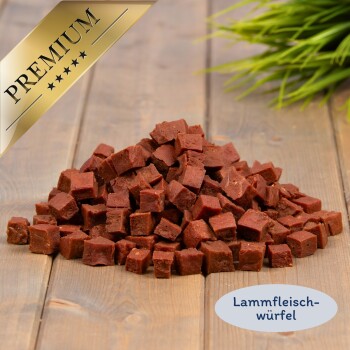 Haufen Lammfleischwürfel auf einem Holzbrett mit Pflanze, goldene ‚PREMIUM‘-Schleife und Etikett ‚Lammfleisch-Würfel‘
