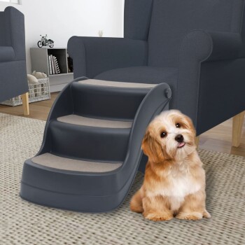 Ein kleiner Hund sitzt neben einer dreistufigen Haustiertreppe in einem gemütlichen Wohnzimmer, mit einem dunkelblauen Sessel und einem hellen Teppich.