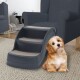 Ein kleiner Hund sitzt neben einer dreistufigen Haustiertreppe in einem gemütlichen Wohnzimmer, mit einem dunkelblauen Sessel und einem hellen Teppich.
