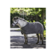 Ein kleiner grauer Pony, das eine angepasste graue Decke trägt, steht auf einem Weg, umgeben von Grün, und zeigt sein Geschirr und sein ruhiges Wesen.