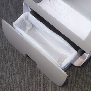 Eine Nahaufnahme eines offenen Haustierabfallentsorgungsbehälters mit einer weißen Kunststoffauskleidung, vor einem grauen Teppichhintergrund.