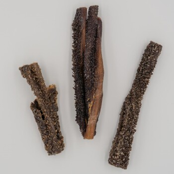 Drei strukturierte Hundekauartikel in unterschiedlichen Längen und Formen, mit einer dunklen, rauen Oberfläche vor einem hellen Hintergrund.