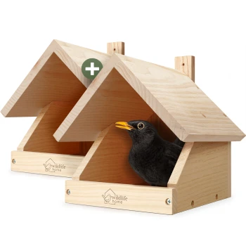 Zwei helle Holzvogelhäuser mit 'wildlife home'-Logo; eine Amsel lugt aus dem vorderen Haus und ein grünes Plus-Abzeichen ist sichtbar