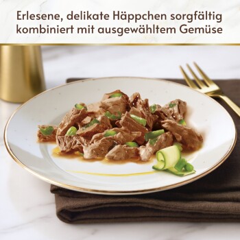 Teller mit Tierfutterstücken aus braunem Fleisch und grünem Gemüse auf einem Teller mit Goldrand; Text: ‚Erlesene, delikate Häppchen…‘