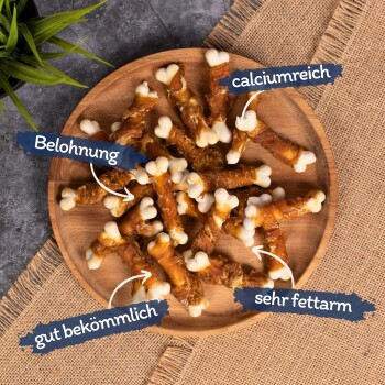 Ein Holzbrett mit hundeknochenförmigen Leckerlis, beschriftet auf Deutsch: "Belohnung," "gut bekömmlich," "calciumreich," und "sehr fettarm."
