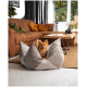 Ein flauschiger Pomeranian sitzt auf einem grauen, blumenförmigen Hundebett in einem gemütlichen Wohnzimmer mit einem braunen Sofa und großen Fenstern.