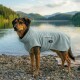Ein gestromter Hund, der einen weichen, hellgrauen Fleece-Mantel trägt, steht vor einem blassblauen Hintergrund und schaut nach oben.