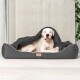 Ein großer weißer Hund liegt bequem in einem grauen Haustierbett, teilweise mit einer Decke bedeckt, vor einem minimalistischen Hintergrund.