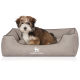 Flauschiger braun-weißer Welpe sitzt in einem grauen rechteckigen Hundebett mit KNUFFELWUFF-Logo