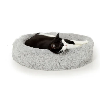 Eine schwarz-weiße Katze, die bequem auf einem weichen, runden grauen Haustierbett liegt.