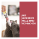 Zwei graue Katzen lecken an einer von einer Hand gehaltenen Tube GimCat DUO Paste; sichtbarer Text: "MIT LECKEREM MALZ UND HÜHNCHEN".