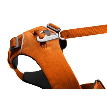 Nahaufnahme eines orangefarbenen Hundegeschirrs mit einem Metallclip und verstellbaren Riemen, das den Markennamen 'RUFFWEAR' trägt.