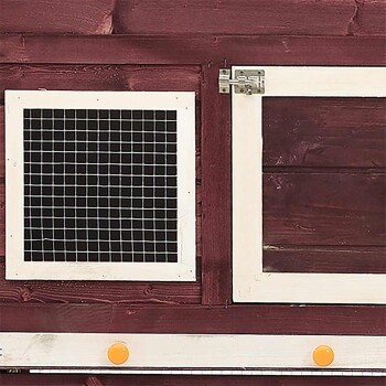 Nahaufnahme eines hölzernen Haustiergeheges mit einem weiß gerahmten Drahtgitterfenster und einer soliden Tür mit Riegel, vor einem roten Holz-Hintergrund.