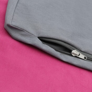 Nahaufnahme eines grauen Haustierbettes mit einem Reißverschluss, das auf einer rosa Oberfläche ruht.