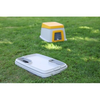 Outdoor-Haustierhaus mit gelbem Dach und weißem Kunststoffsockel auf grünem Gras, Deckel abgenommen und daneben liegend.