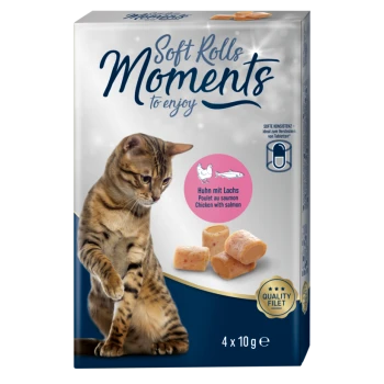 Un chat tigré est assis à côté d'un paquet de friandises pour chats "Soft Rolls Moments", avec des saveurs de saumon et de poulet, contenant quatre portions de 10 g.