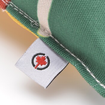 Nahaufnahme eines bunten Haustier-Spielzeugs mit einer grünen Stoffoberfläche und einem Etikett mit einem roten Ahornblatt-Logo.