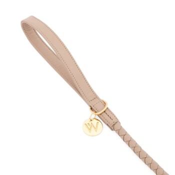 Eine stilvolle beige Hundeleine mit einem geflochtenen Design und einem goldenen runden Anhänger mit dem Buchstaben 'W.'