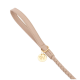 Eine stilvolle beige Hundeleine mit einem geflochtenen Design und einem goldenen runden Anhänger mit dem Buchstaben 'W.'