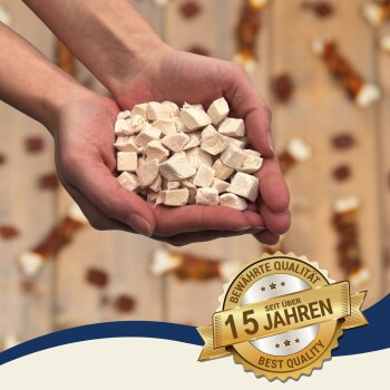 Hände, die weiße, in Würfel geschnittene Tierleckerlis halten, unscharfer Hintergrund, goldenes Siegel mit der Aufschrift „Seit über 15 Jahren“