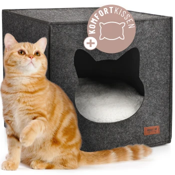 Orange getigerte Katze sitzt neben einem grauen Filz-Katzenhaus mit katzenförmigem Eingang und dem Text „Komfort Kissen“.