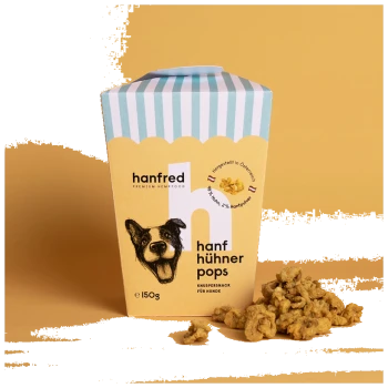 Eine bunte Verpackung von "hanf hühner pops" Hundeleckerlis, mit einer Illustration des Gesichts eines Hundes, mit einigen Leckerlis, die daneben verstreut sind.