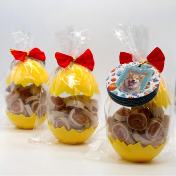 Drei durchsichtige Beutel mit runden Hundeleckerlis in gelben, eiförmigen Behältern mit Rissen, gebunden mit roten Schleifen, beschriftet mit „Therpa Osterei“.