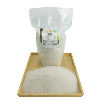 Eine durchsichtige Plastiktüte mit Badesand, beschriftet mit "Nager Badesand", steht aufrecht auf einem Holztablett, mit einem Sandhaufen davor.