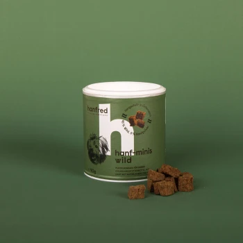 Ein zylindrischer Behälter mit "hanf-minis wild" Hundeleckerlis, mit einem grünen Etikett mit einer Hundillustration, umgeben von kleinen braunen Leckerli-Würfeln.